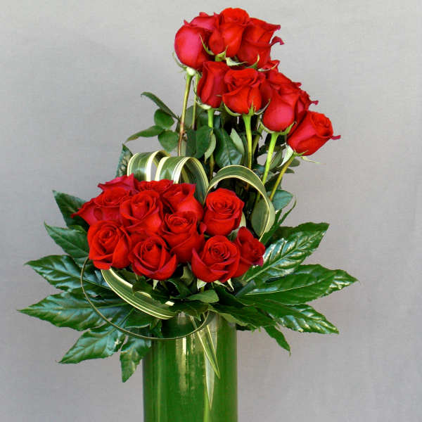 Red roses arranged in a tall green vase with decorative ribbon loops
