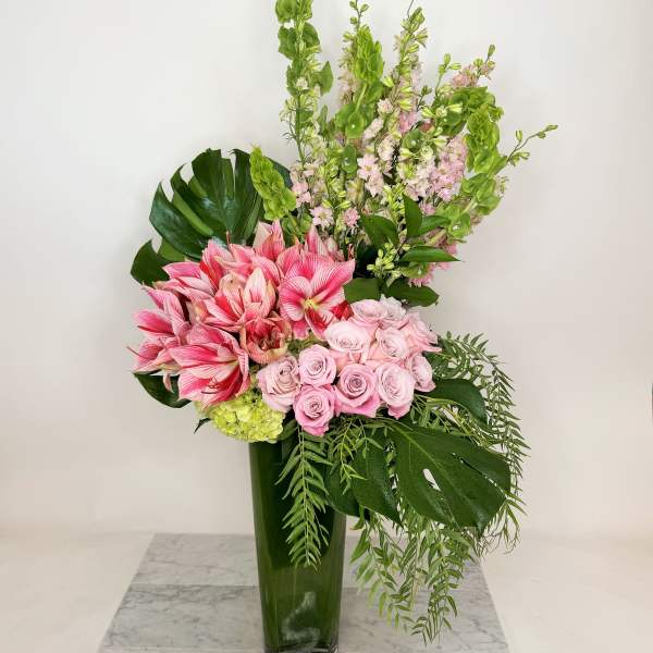 Pink roses and amaryllis in a tall green vase with tropical foliage