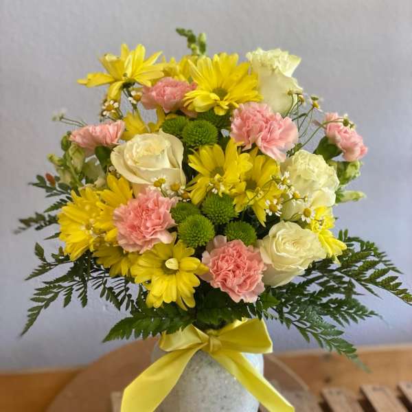 Bouquet of yellow and pink flowers in a white vase with a yellow ribbon