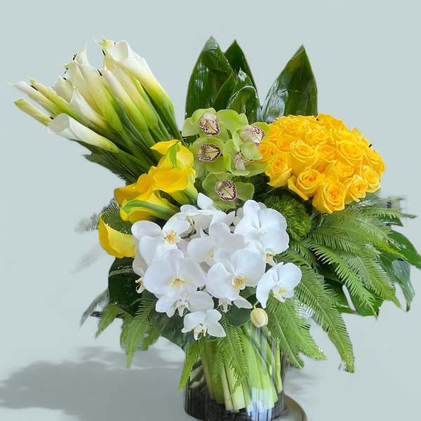 Bouquet of yellow roses, white orchids, and calla lilies in a glass vase