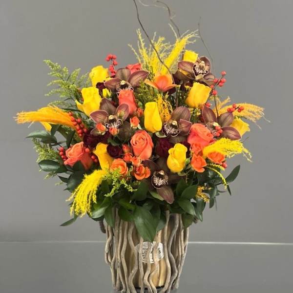 Bouquet of yellow and coral roses with orchids in a decorative vase