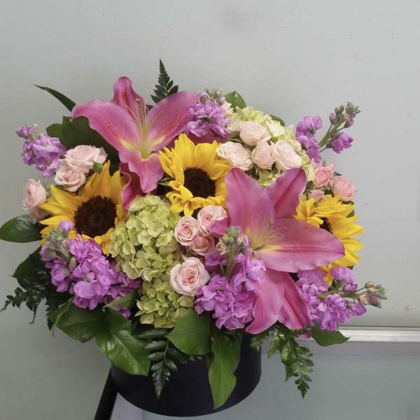 Pink lilies and sunflowers in a black hatbox with pastel roses