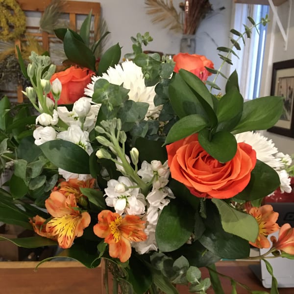 Bouquet of orange roses, white flowers, and orange alstroemeria in a glass vase