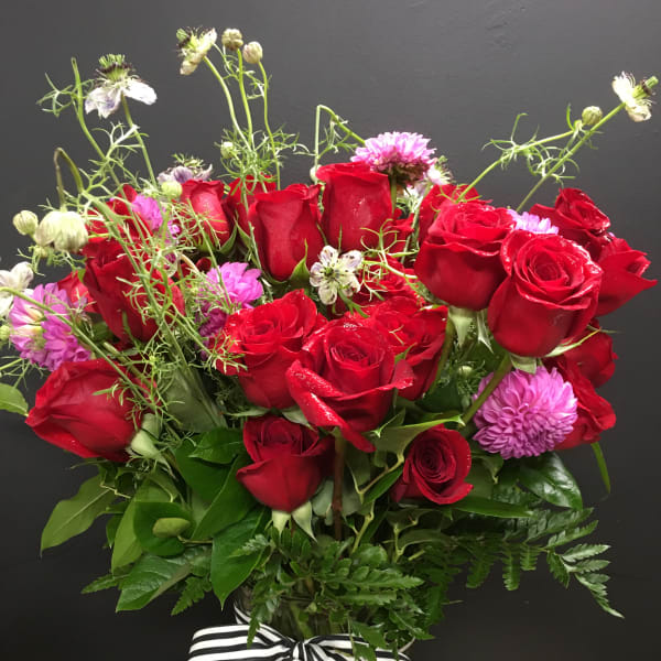 Bouquet of red roses and pink flowers in a glass vase with a striped ribbon