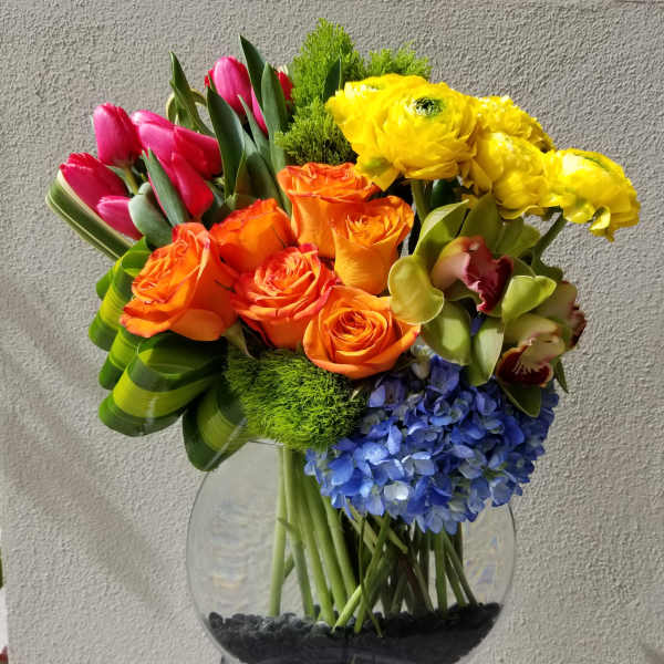 Colorful bouquet of tulips, roses, orchids, hydrangea, and yellow blooms in a glass vase