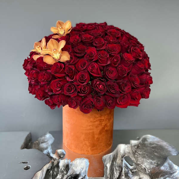 Red rose arrangement in an orange velvet vase with peach orchids