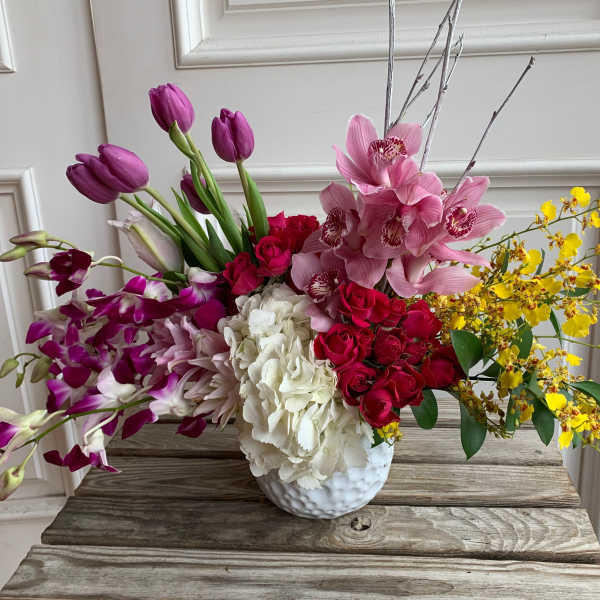 Mixed bouquet in a white vase with pink orchids, red roses, white hydrangea, and yellow sprays