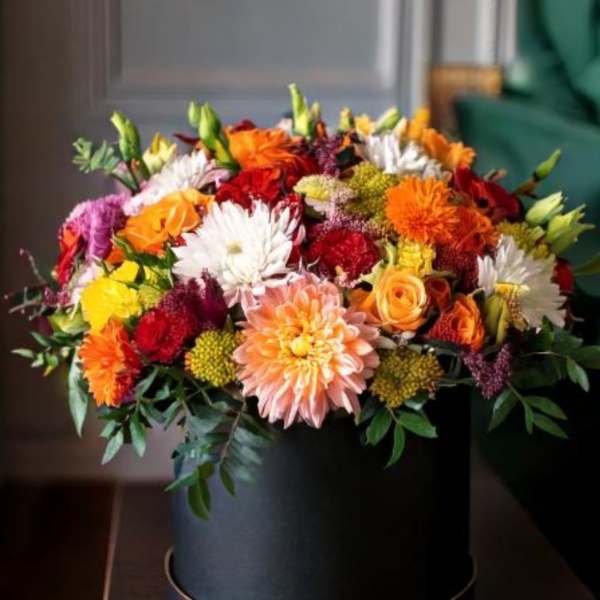 Mixed bouquet in a black round box with orange, red, white, and pink blooms