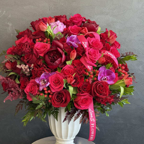 Large red rose arrangement in a white vase with pink orchids