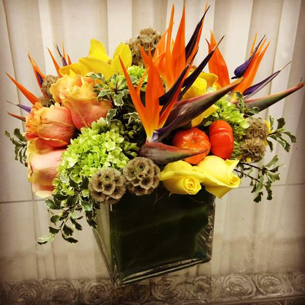 Tropical bouquet with orange bird-of-paradise and yellow roses in a square vase