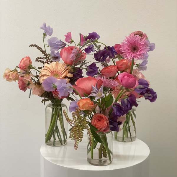 Three colorful flower bouquets in clear glass vases on a white table