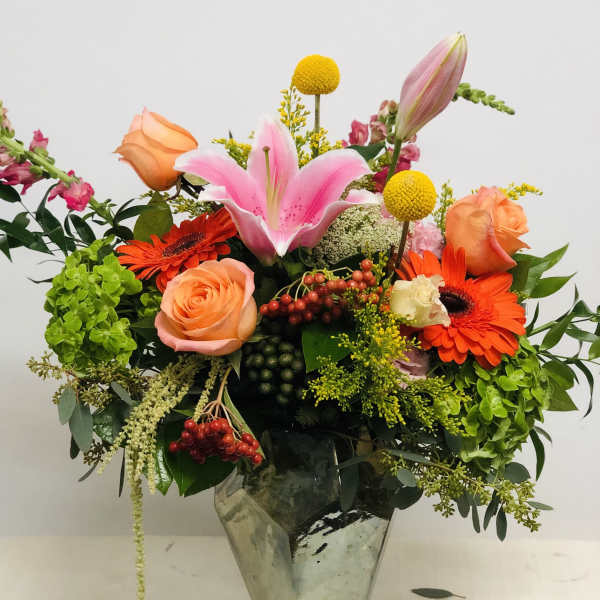 Mixed bouquet with pink lily, orange roses, and gerbera daisies in a glass vase