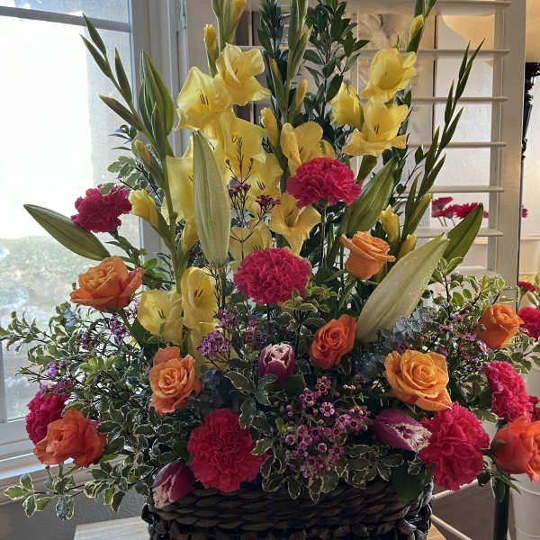 Tall mixed flower arrangement in a woven basket with yellow lilies and orange roses