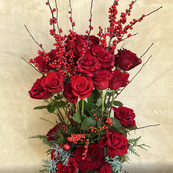 Tall arrangement of red roses with berry branches in a gold vase
