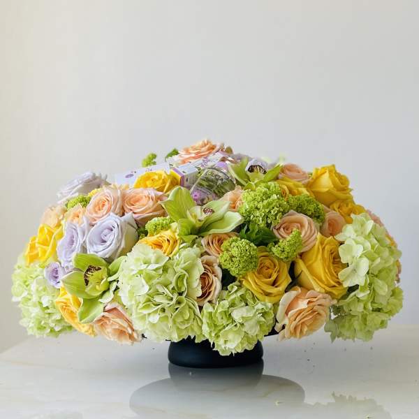 Low floral arrangement with roses, hydrangeas, and orchids in a black vase