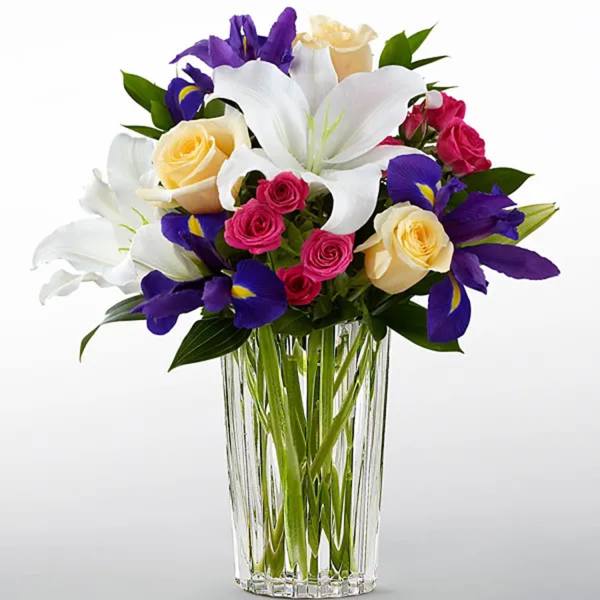 Bouquet of white lilies, purple irises, and pink and yellow roses in a glass vase