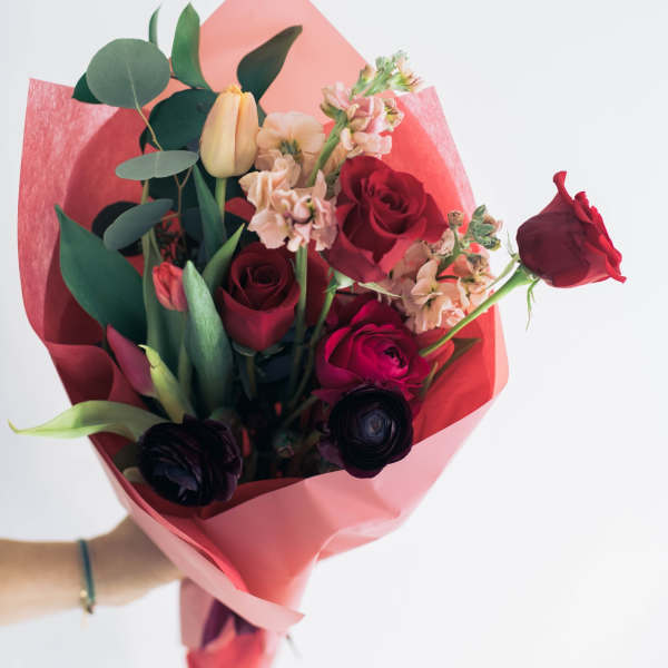 Bouquet of red roses, tulips, and pale pink flowers wrapped in pink paper