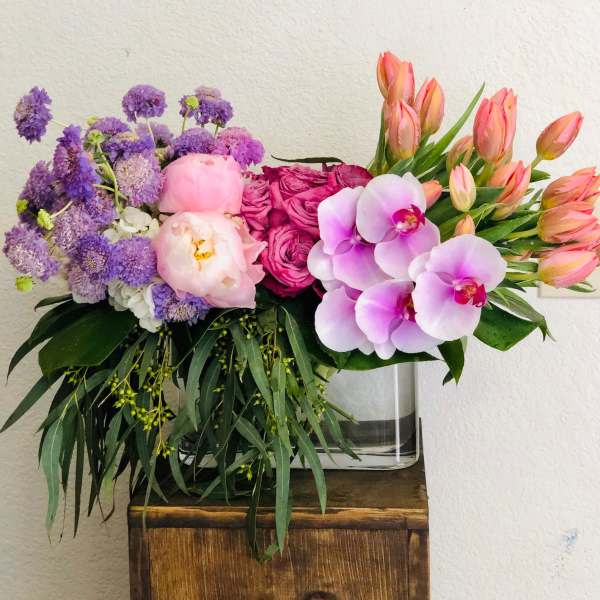 Colorful bouquet with purple blooms, pink roses, orchids, and tulips in a glass vase