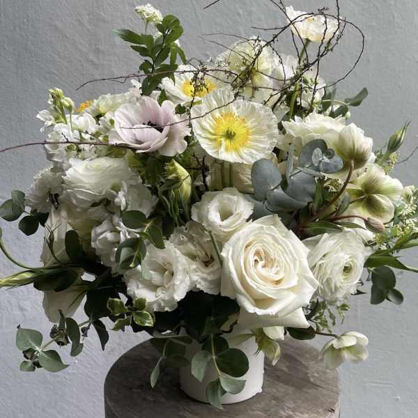 White floral arrangement in a white vase with roses and poppy-like blooms
