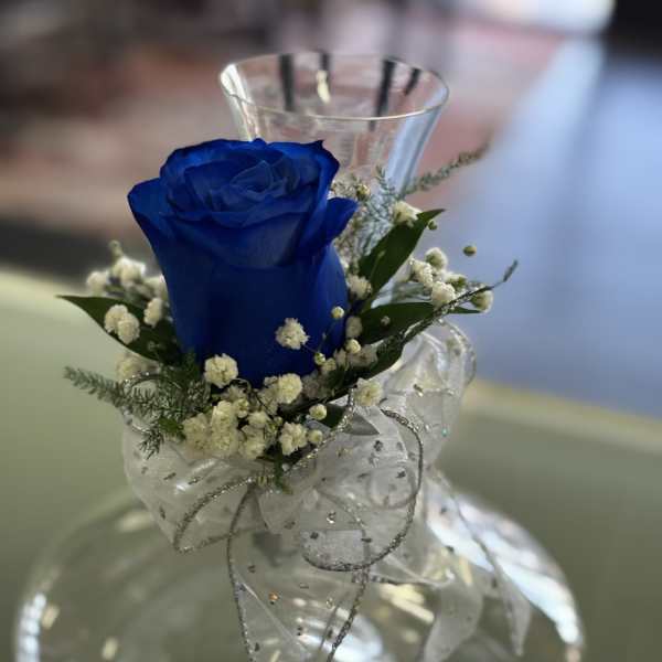 Single blue rose with white accent flowers and silver ribbon in a clear glass vase