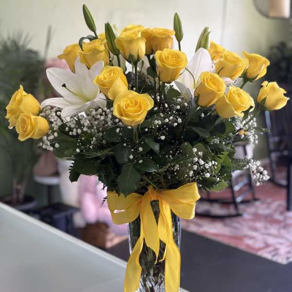 Yellow roses and white lilies in a clear glass vase with a yellow ribbon