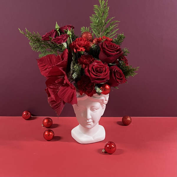 Red roses arranged in a white bust vase with holiday ornaments