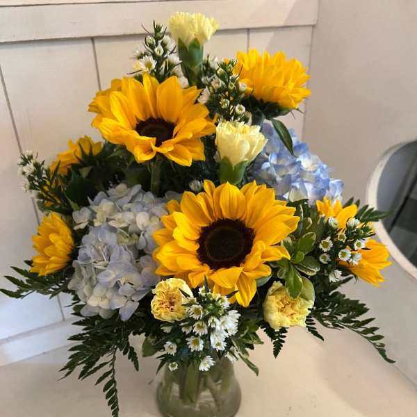 Bouquet of sunflowers, hydrangeas, and small white flowers in a glass vase