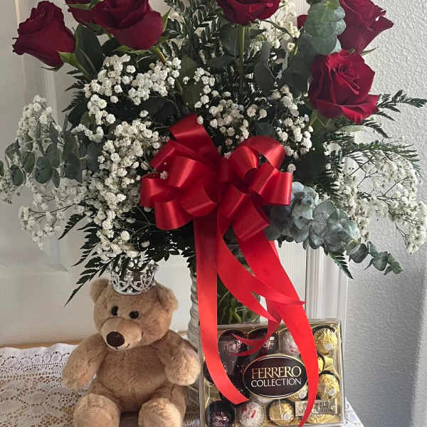 Red roses in a vase with baby’s breath, a teddy bear, and chocolates
