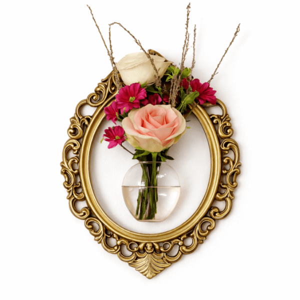 Small floral arrangement in a clear wall vase inside an ornate gold frame
