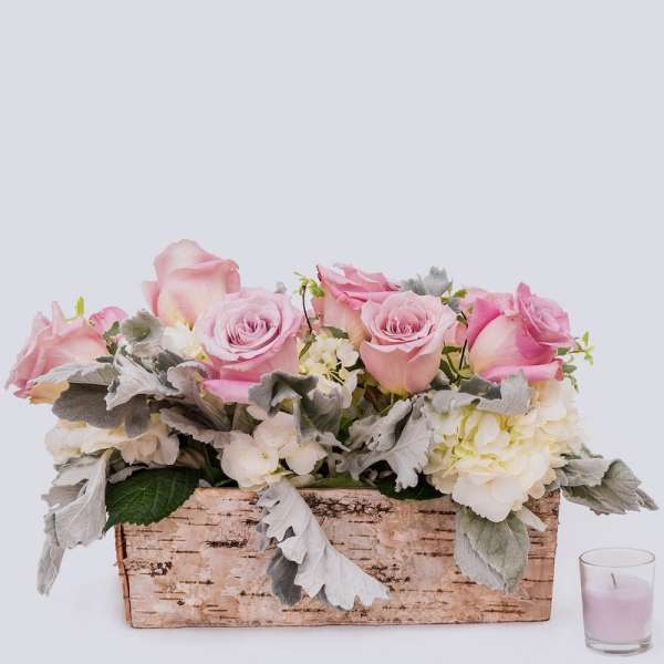 Pink roses and white hydrangeas in a birch bark container with a small candle