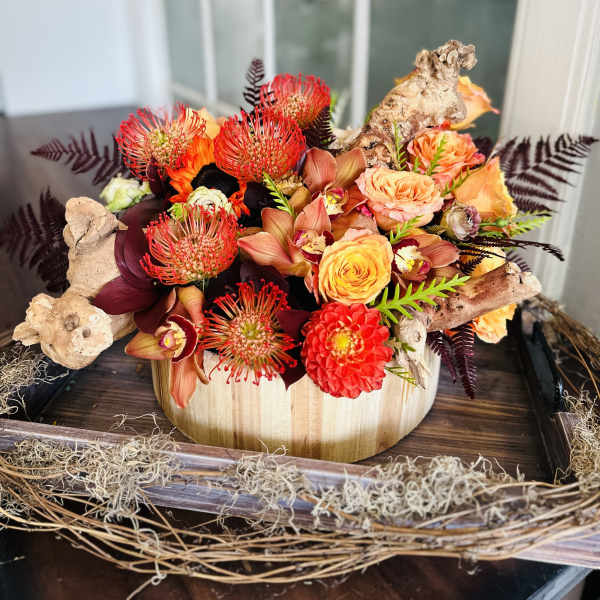 Orange and red floral arrangement in a wooden container with driftwood accents