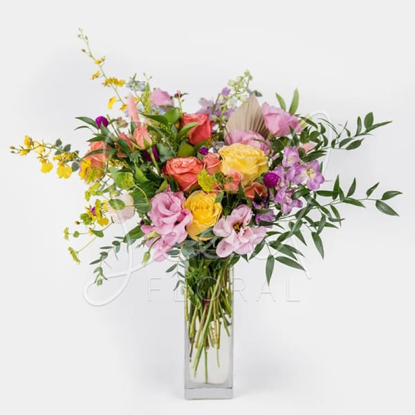 Tall mixed bouquet of pink, yellow, and peach flowers in a clear rectangular glass vase