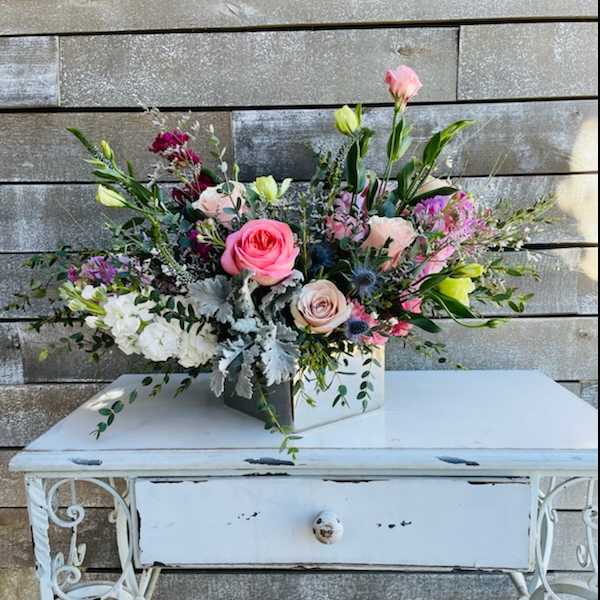 Mixed pink and white floral arrangement in a square container on a white table