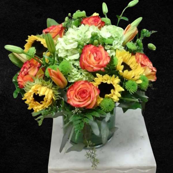 Bouquet of orange roses, yellow sunflowers, and white hydrangeas in a glass vase