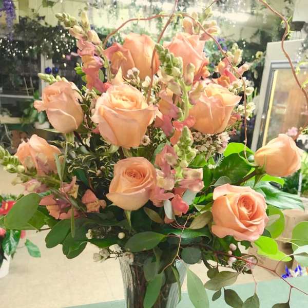 Peach roses arranged in a clear glass vase with pink snapdragons