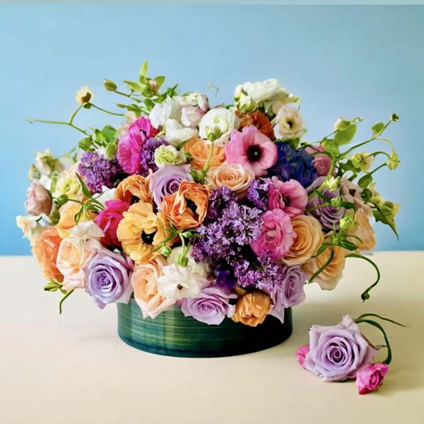 Mixed bouquet of pastel roses and other flowers in a green vase
