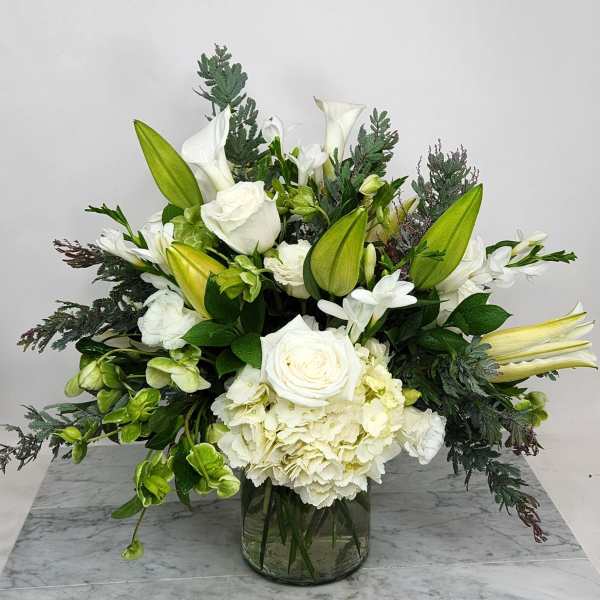 White floral arrangement with lilies, roses, and hydrangea in a glass vase