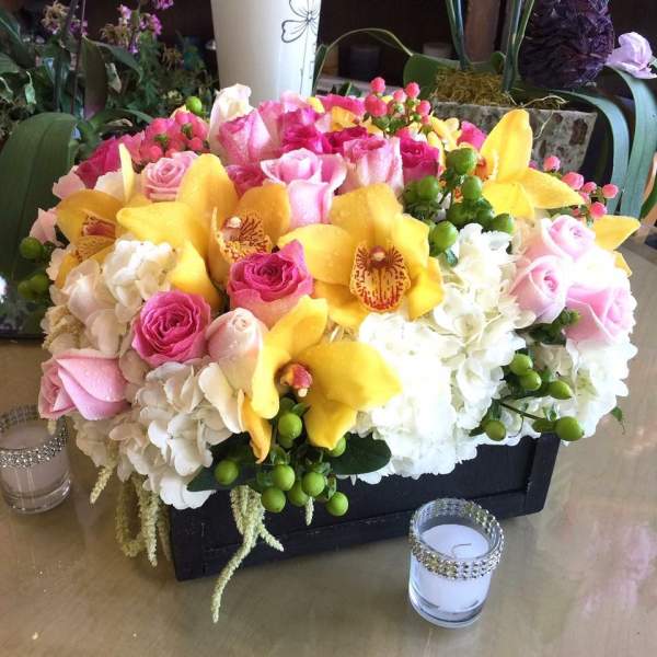 Pink roses and yellow orchids arranged in a black rectangular container