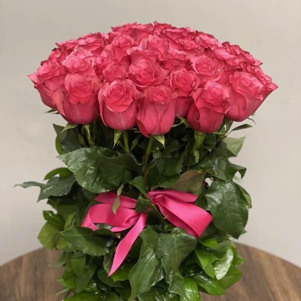 Tall arrangement of bright pink roses with a matching ribbon in a rustic wooden vase