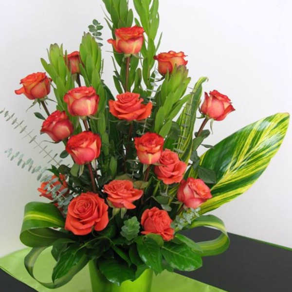 Arrangement of orange roses in a bright green pot with tall green accents and striped leaves
