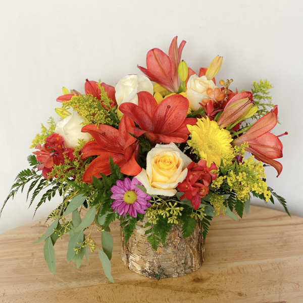 Colorful flower arrangement in a birch bark container with red lilies and roses