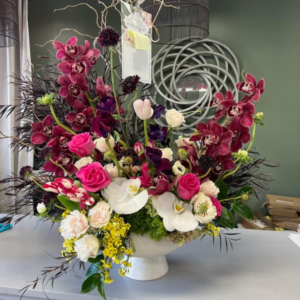 Large floral arrangement with orchids, roses, and tulips in a white pedestal vase
