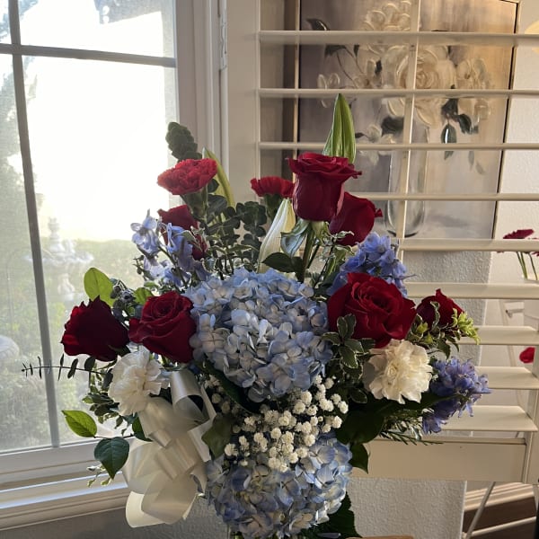 Mixed bouquet of red roses, blue hydrangeas, and white flowers in a glass vase