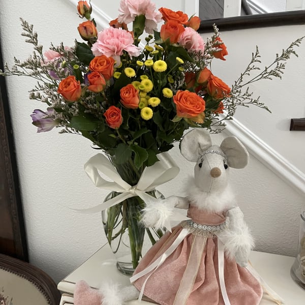 Bouquet of orange and pink roses with yellow button flowers in a glass vase