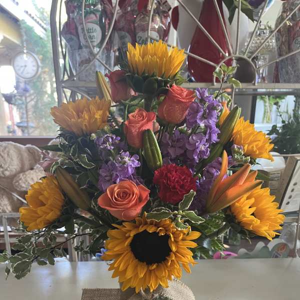 Mixed bouquet with sunflowers, roses, lilies, and purple blooms in a glass vase