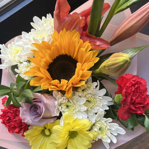 Bright mixed bouquet with sunflower, lilies, carnations, roses and daisies wrapped in pink paper
