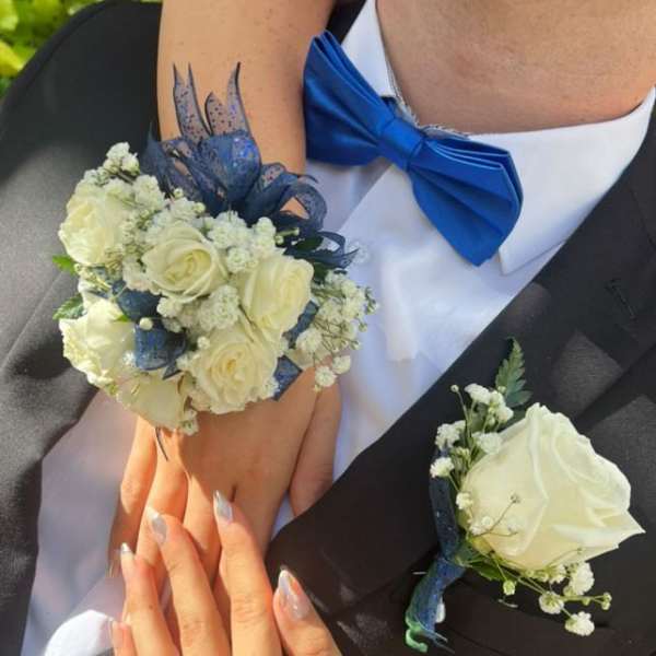 White rose wrist corsage and matching boutonniere with blue ribbon on a couple in formalwear