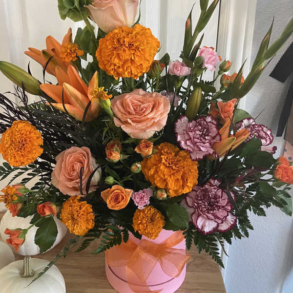 Orange and peach floral arrangement in a pink hatbox with ribbon