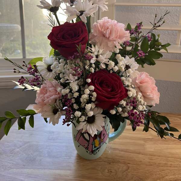 Mixed bouquet of red roses, pink carnations, and white daisies in a mug
