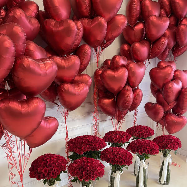 Red heart balloons above bouquets of red roses in glass vases